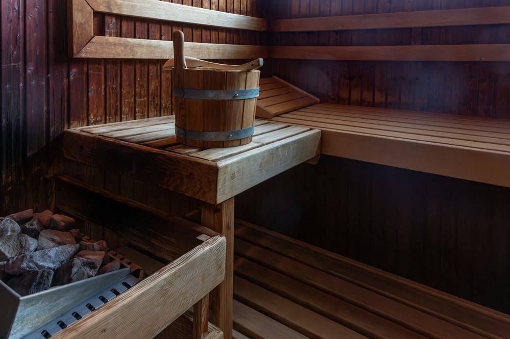 Interior of a Wooden Sauna With a Bucket, Bench, and Heating Stones Visible — Intouch Pools & Spas in Forster, NSW