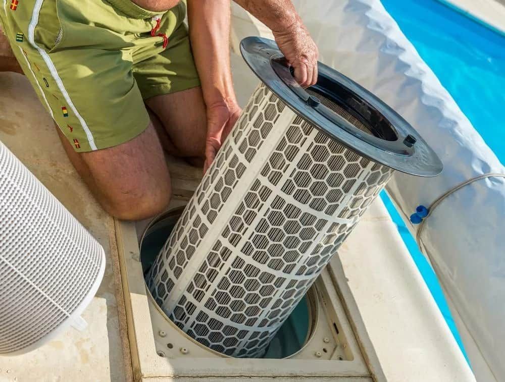 A Man is Kneeling Down to Remove a Filter From a Swimming Pool — Intouch Pools & Spas in Forster, NSW