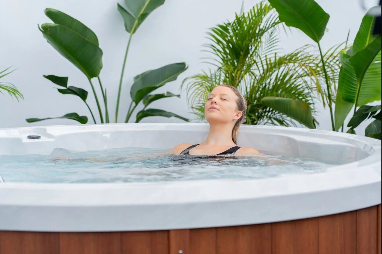 Woman relaxing in a hot tub, eyes closed, surrounded by green plants and a white wall. — Intouch Pools & Spas in Tuncurry, NSW