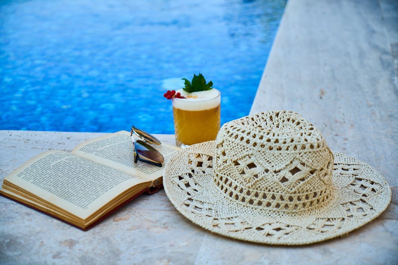 Straw Hat, Open Book With Silver Bookmark, and Cocktail Near a Pool — Intouch Pools & Spas in Forster, NSW