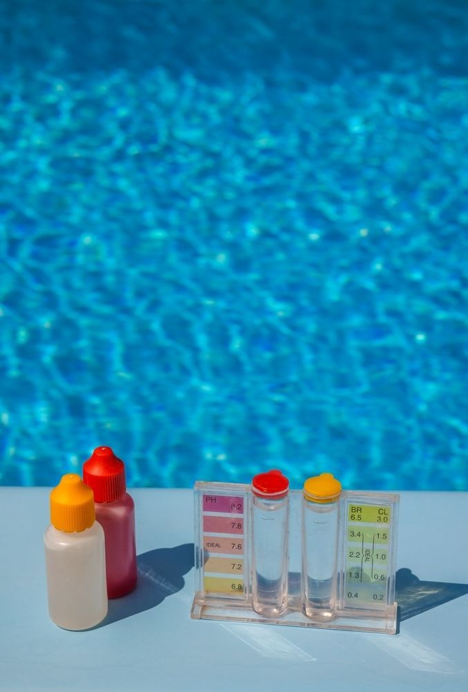 Pool Water Testing Kit With Bottles and Test Tubes With a Blue Pool in the Background — Intouch Pools & Spas in Forster, NSW