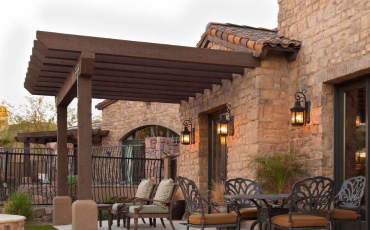 A sophisticated outdoor seating area under a dark wooden pergola adjacent to a rustic stone wall, exuding Tempe's warm elegance.