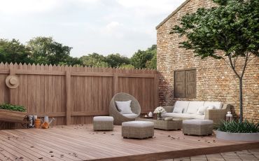 A tranquil deck in Tempe, AZ, featuring modern wicker furniture and plush cushions, framed by a classic wooden fence and mature tree.