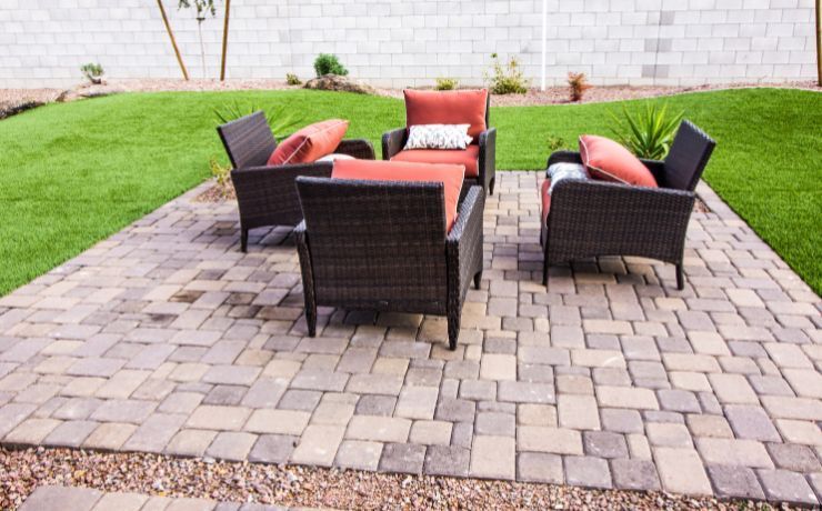 A charming brick patio with rattan furniture and plush cushions, nestled in a neatly landscaped yard in Tempe, Arizona.