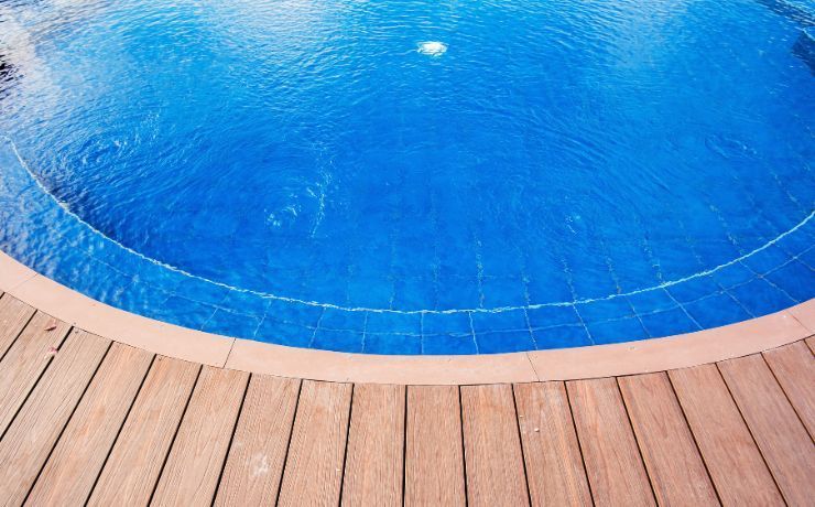 Wooden pool deck curving around a sparkling blue pool, offering a sleek and safe area for poolside relaxation in Tempe.