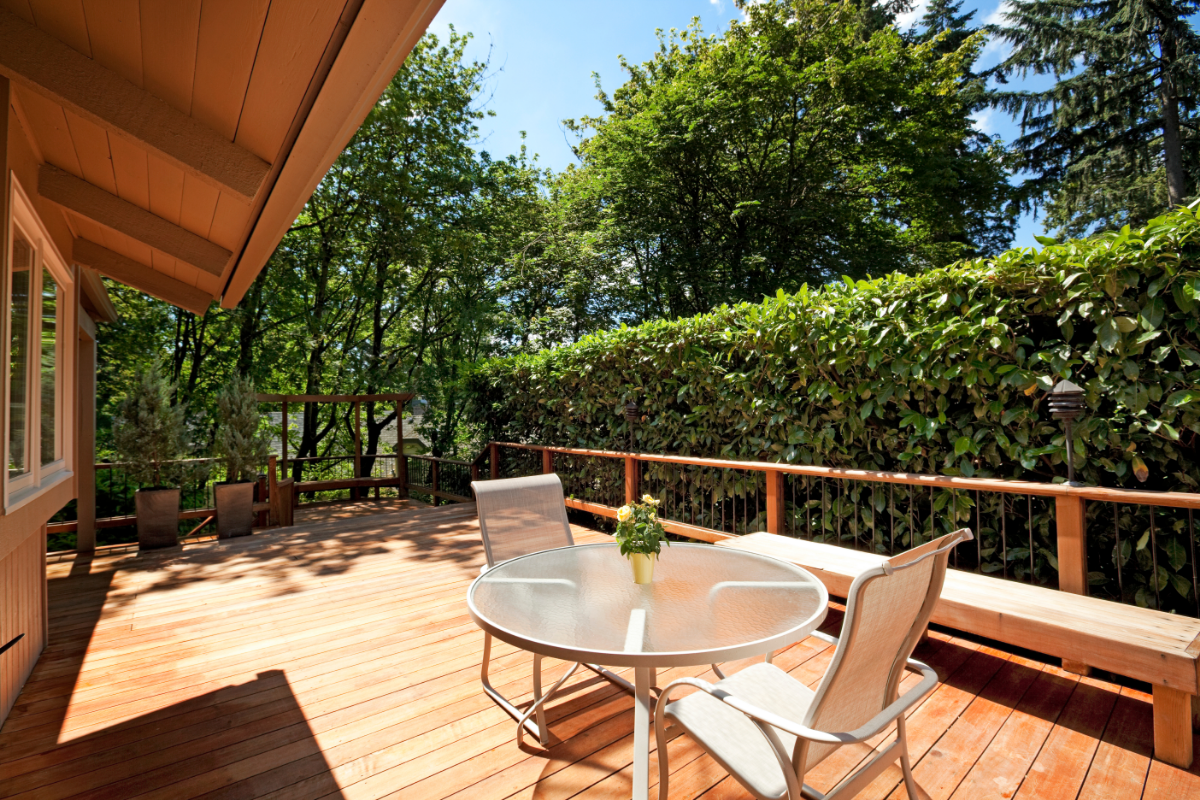 A sunny wooden deck with a table set, surrounded by Tempe greenery, offers an outdoor retreat.