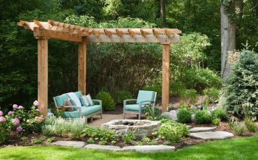 A serene pergola seating area in a lush Tempe garden, complete with comfortable blue cushions and a natural stone fire pit.