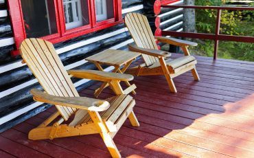 Rustic wooden Adirondack chairs on a dark-stained deck, offering a relaxed outdoor seating area against a cabin-style home in Tempe.