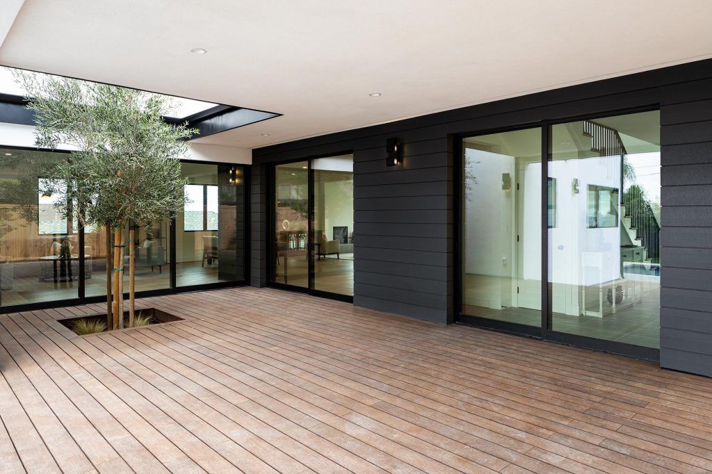 Patio with wooden deck, large glass doors, and a small tree. Dark exterior wall and white ceiling.