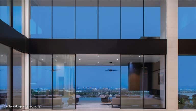 Modern home interior with large glass windows overlooking a cityscape at dusk.