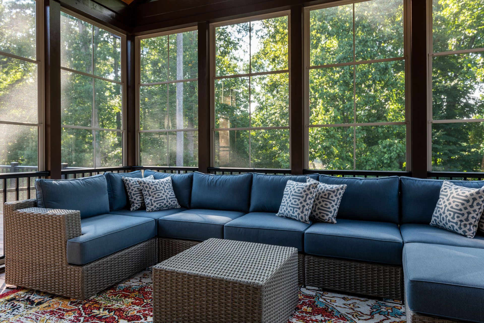 Blue sectional sofa on a screened porch with large windows overlooking trees.
