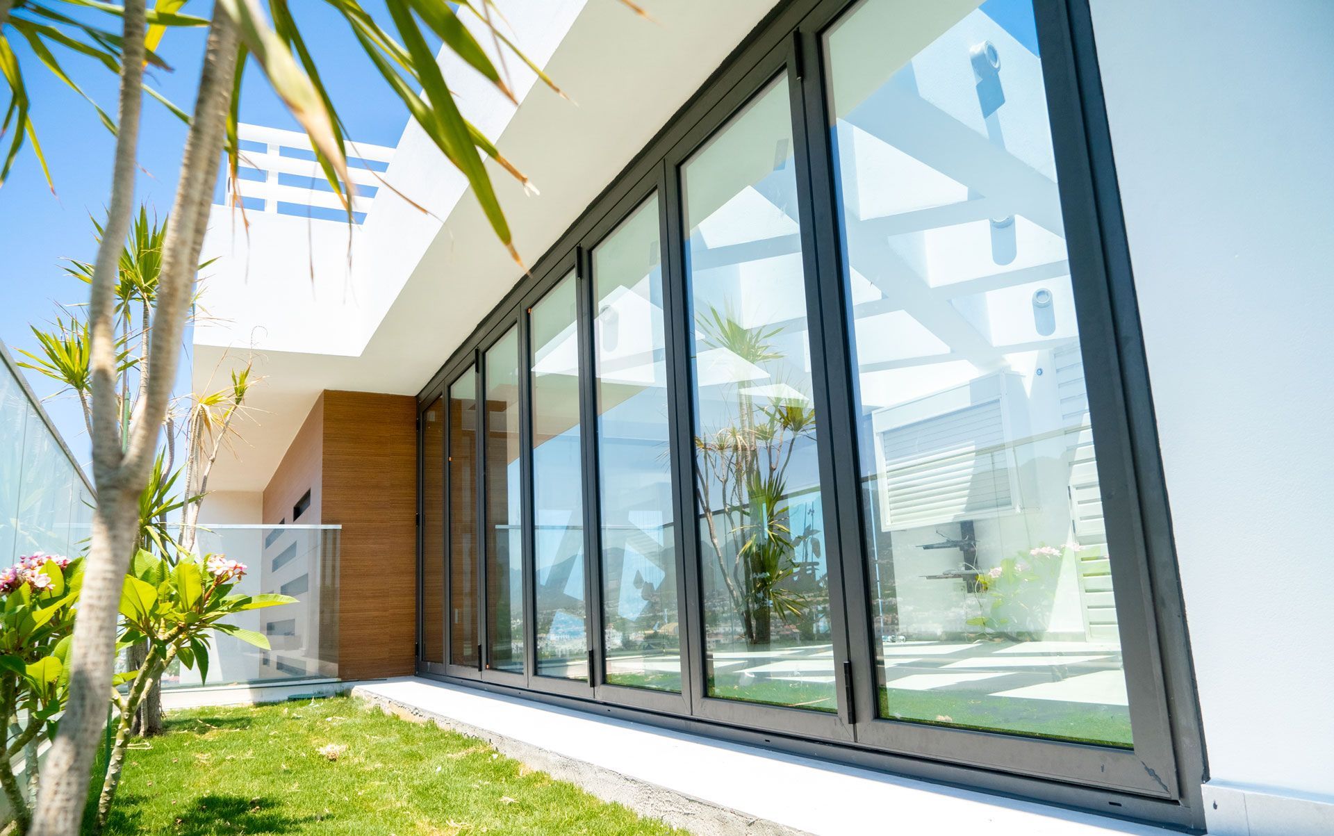 Modern house exterior with large glass doors, green grass, and bright blue sky.