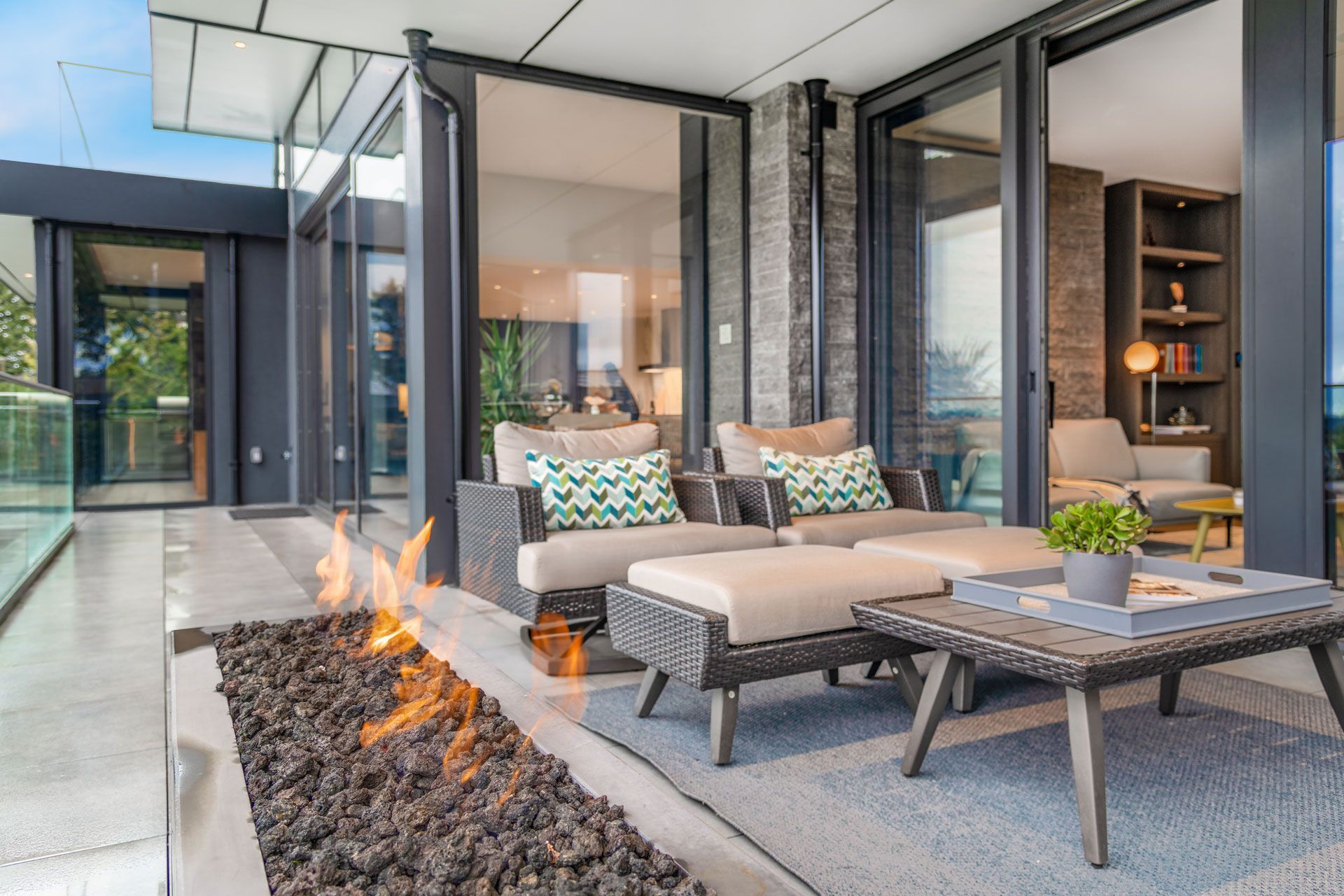 Outdoor patio with seating and a fire pit, facing open glass doors to a room.