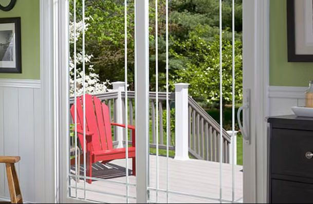Sliding glass door opens to a deck with a red chair; trees in background. Interior: green wall, white trim.