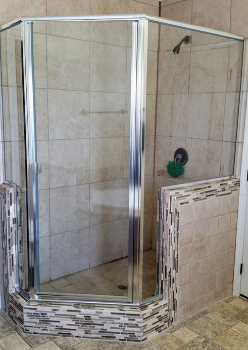 Glass-enclosed shower with beige tile walls and mosaic tile base. Chrome fixtures.
