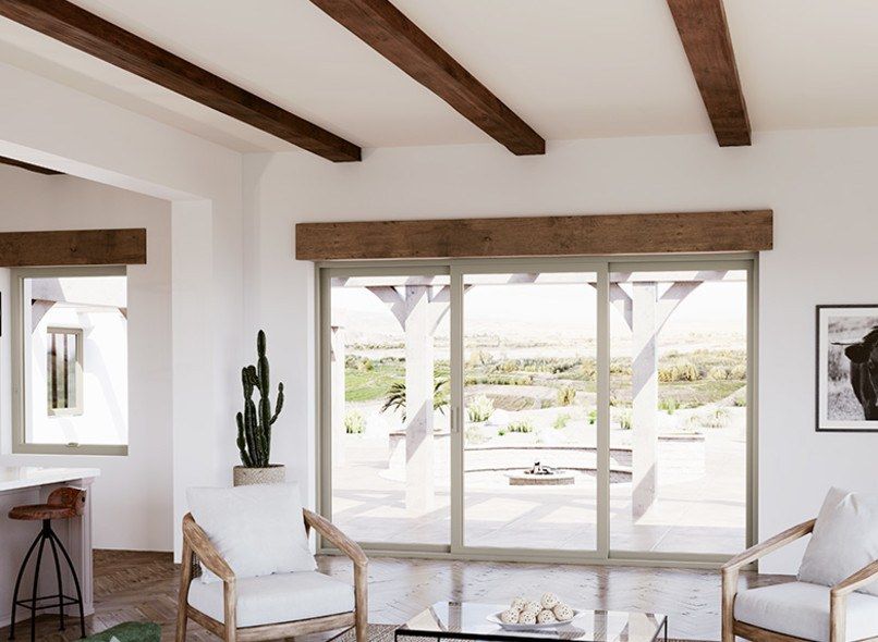 Bright living room with large windows, wood beams, and white chairs overlooking a landscape.