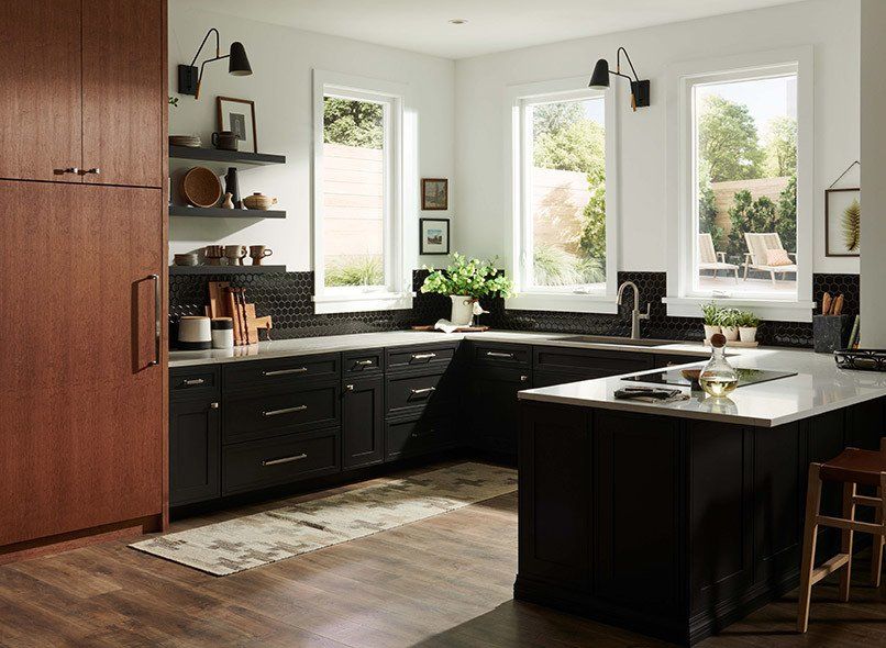 Modern kitchen with black cabinets, brown pantry, white walls, and windows overlooking a backyard.