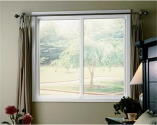 Sliding window in a room, overlooking a yard with a tree, curtains, and a bed.