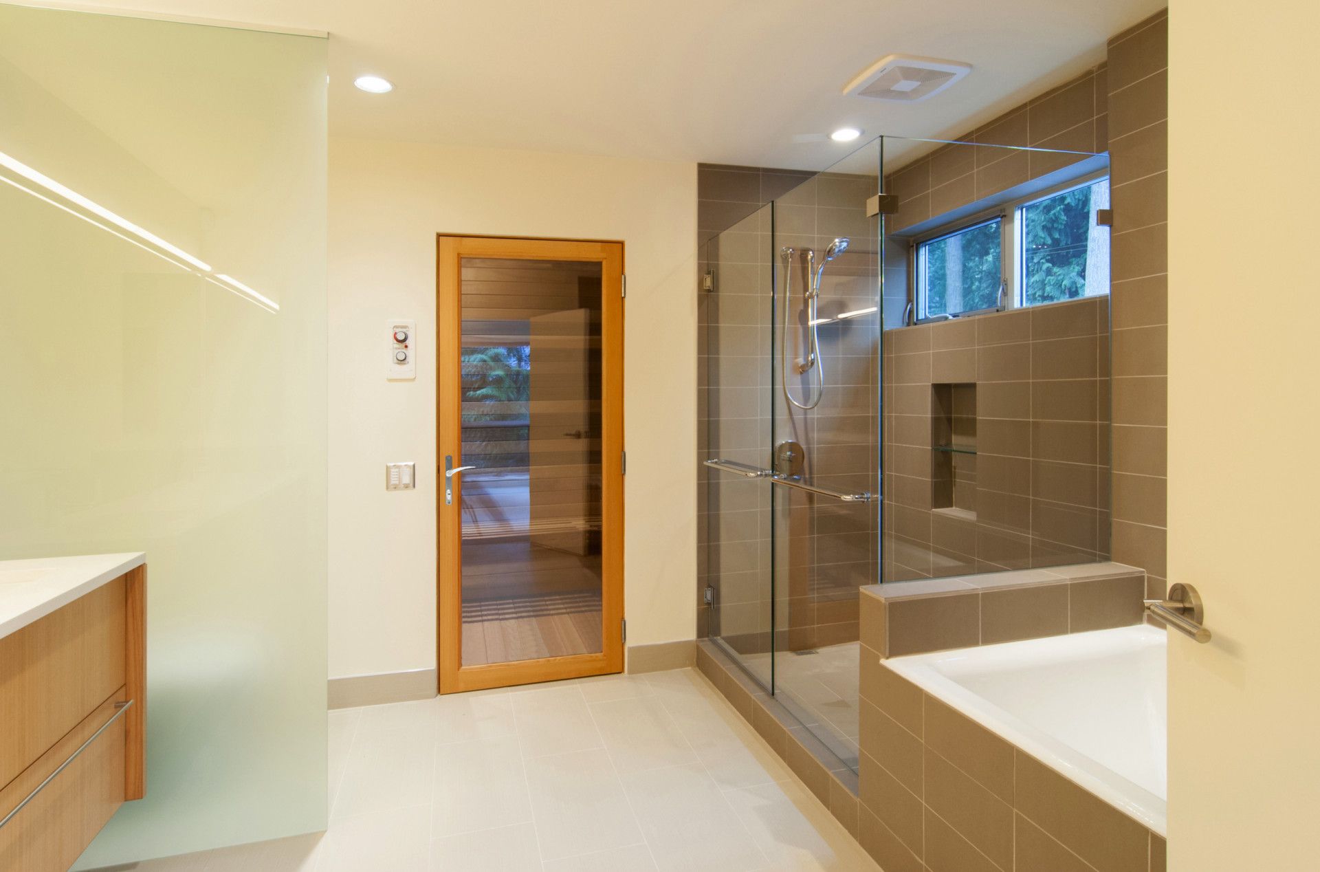 Modern bathroom with a glass shower, bathtub, and wooden door.