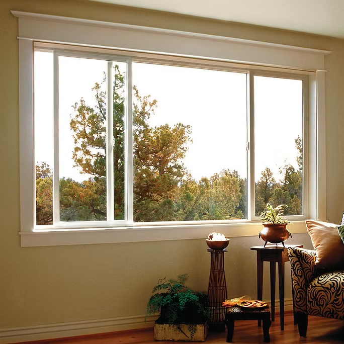 Sliding glass window in a beige-walled room overlooking a bright, tree-filled outdoor scene.