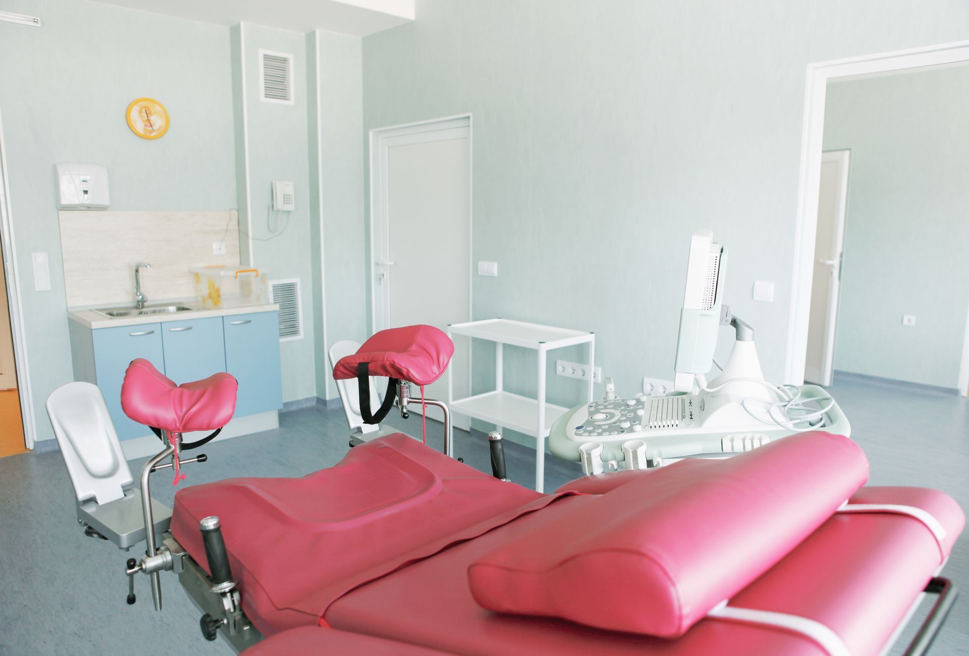 A fuchsia-colored gynecological examination chair in an empty clinic room.