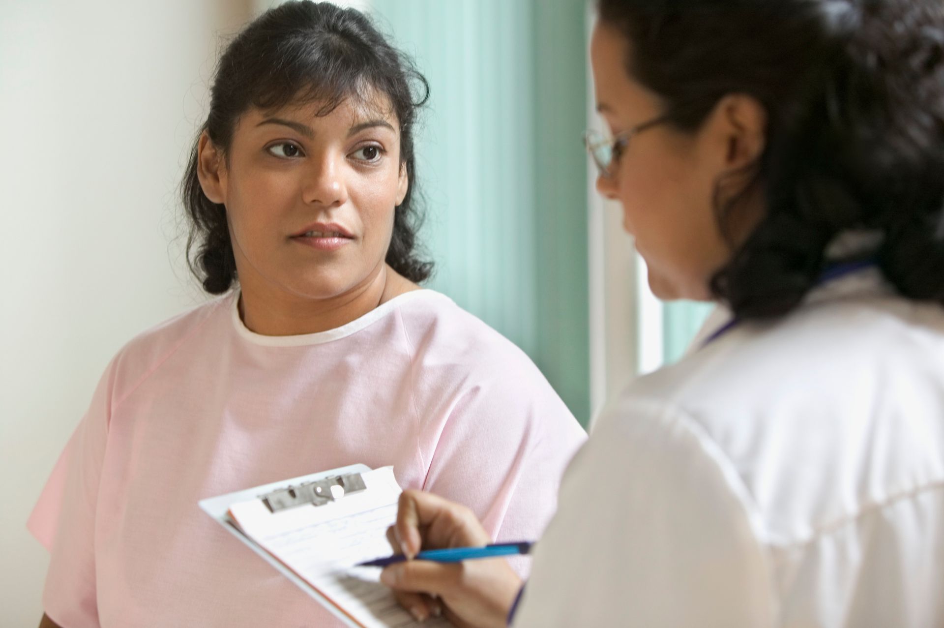 A female doctor writing notes with a female patient watching.
