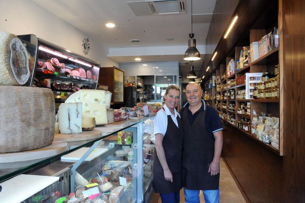 In una gastronomia, i salumi, tra cui salsicce e prosciutti confezionati singolarmente, sono esposti in una cassa di legno e sugli scaffali.