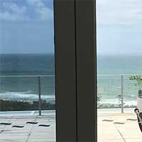 A View Of The Ocean From A Balcony Through A Glass Door — Home Tint Sunshine Coast Window Tinting In Maroochydore, QLD