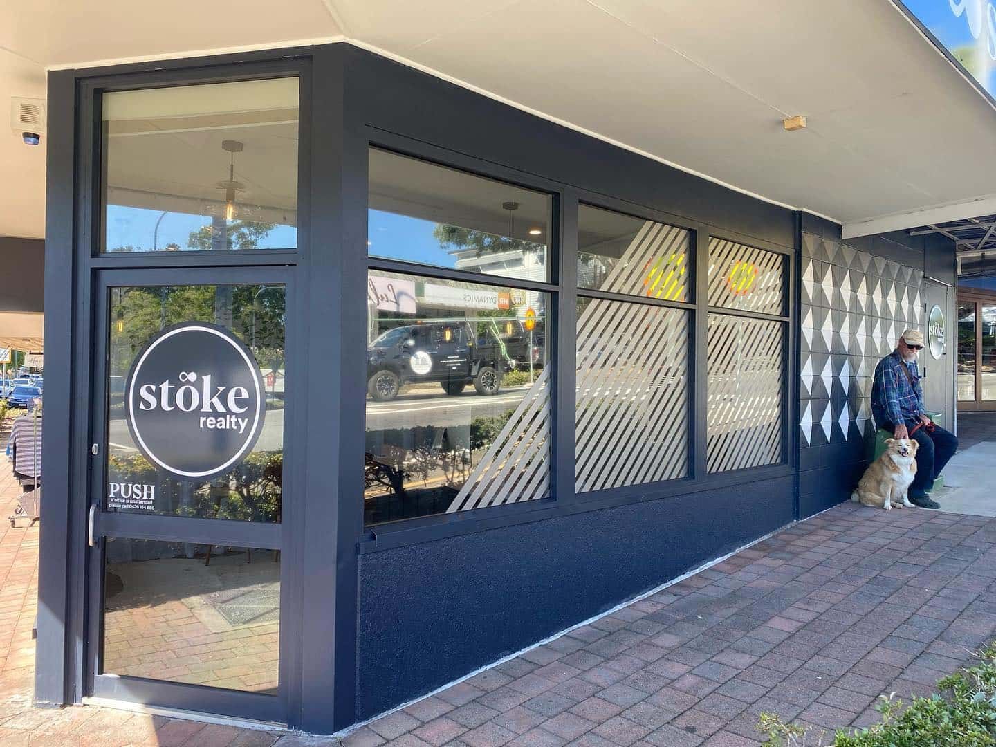 A Man Is Sitting On The Sidewalk In Front Of A Store — Home Tint Sunshine Coast Window Tinting In Maroochydore, QLD