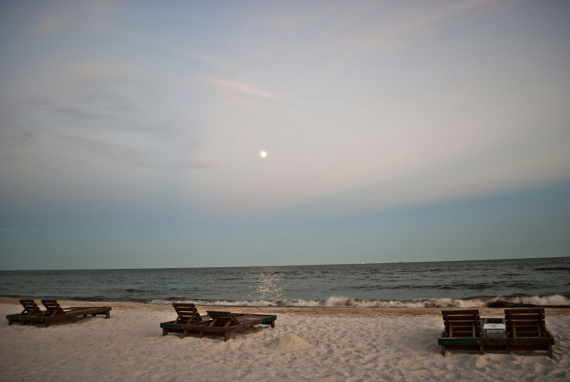 A beach with chairs and a full moon in the sky