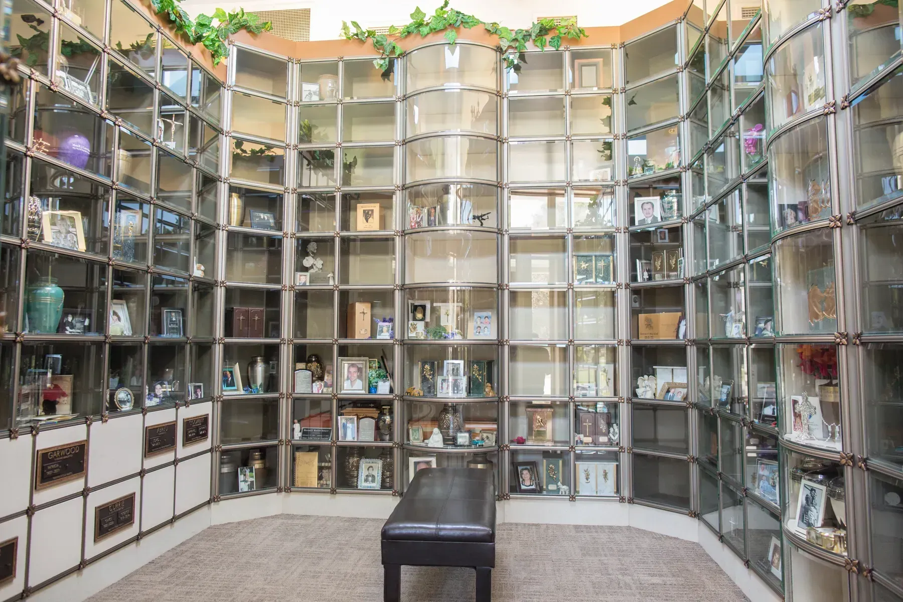 White memorial wall of niches with photos, flowers, and candles in a quiet indoor columbarium