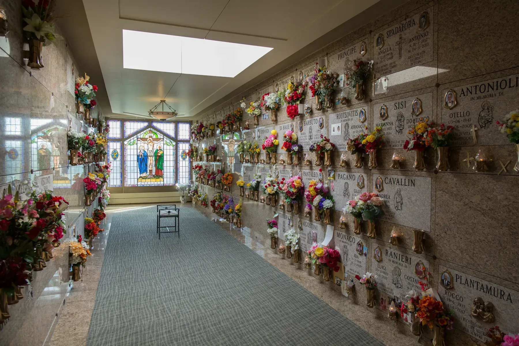 Hallway lined with colorful flower memorials and plaques under bright skylights