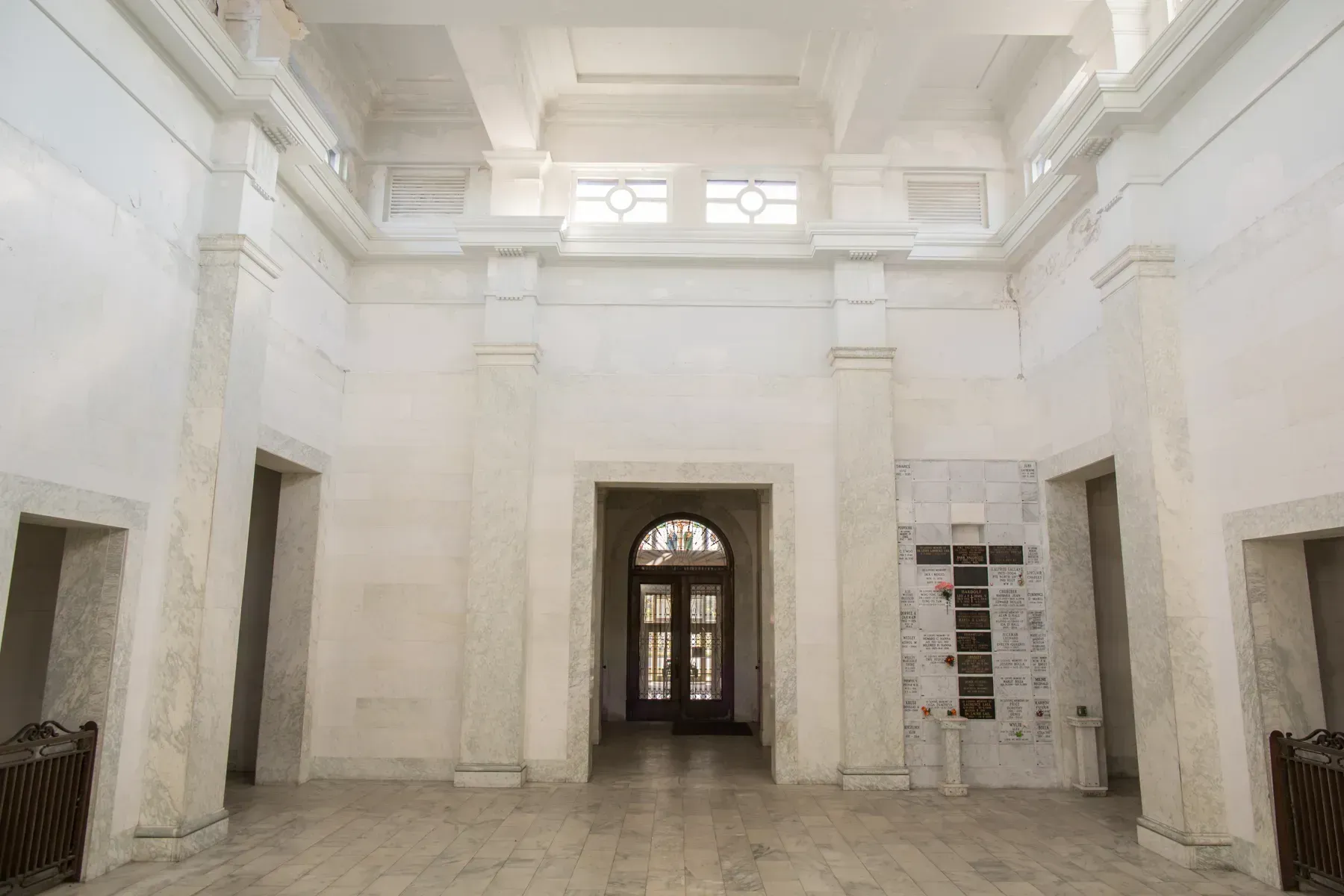 White, empty hall with high ceilings, marble floor, and a central arched doorway