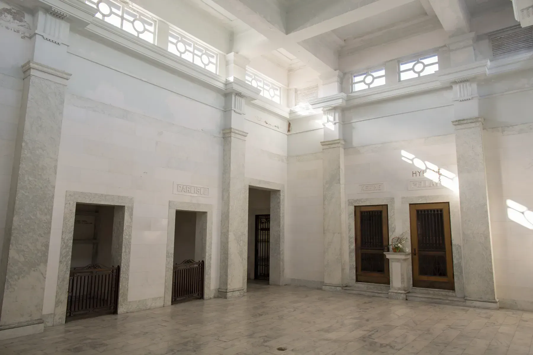 Bright, empty white room with high windows, doorways, and sunlight streaming across the floor.