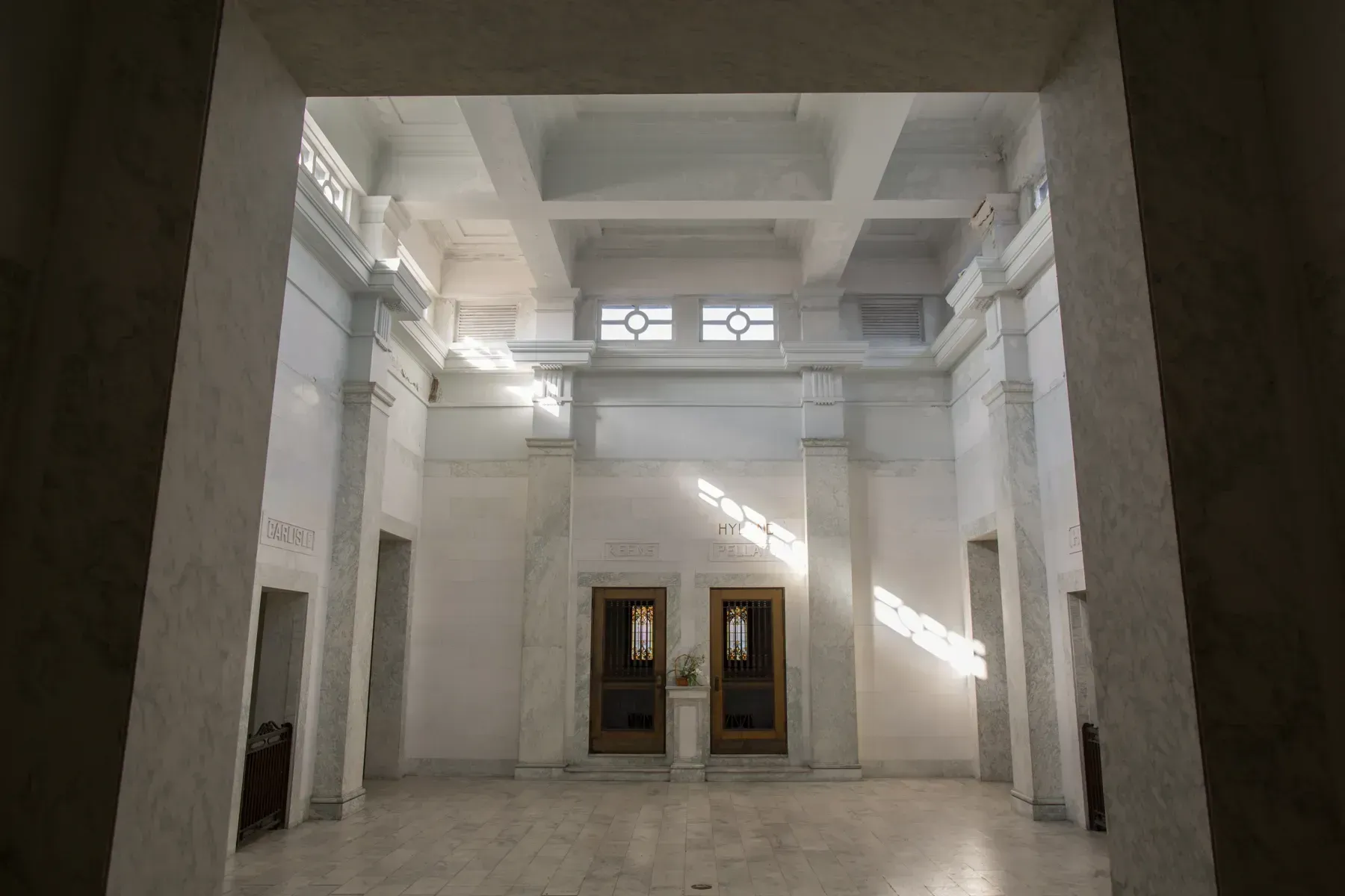Empty grand hall with tall white columns, high windows, and a polished floor.