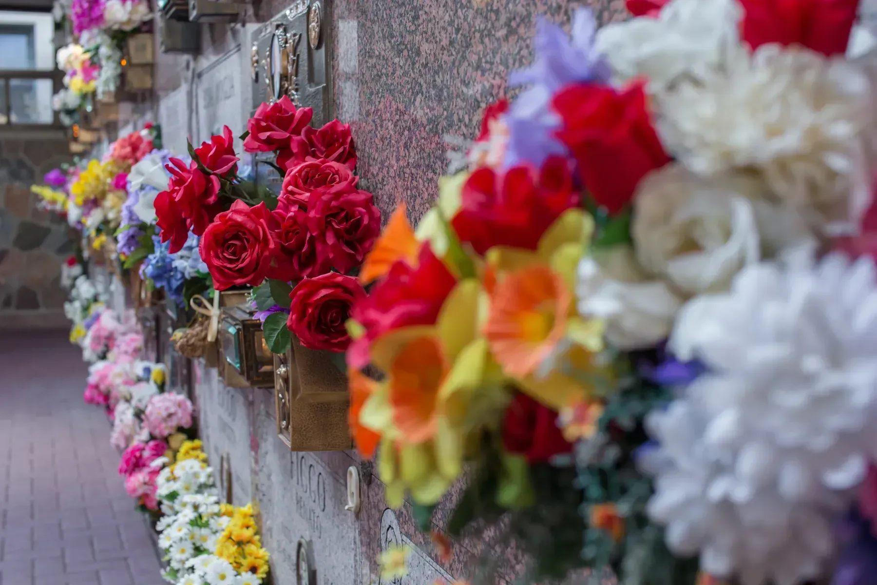 Wall of memorial flowers in bright red, white, pink, and yellow bouquets along a street