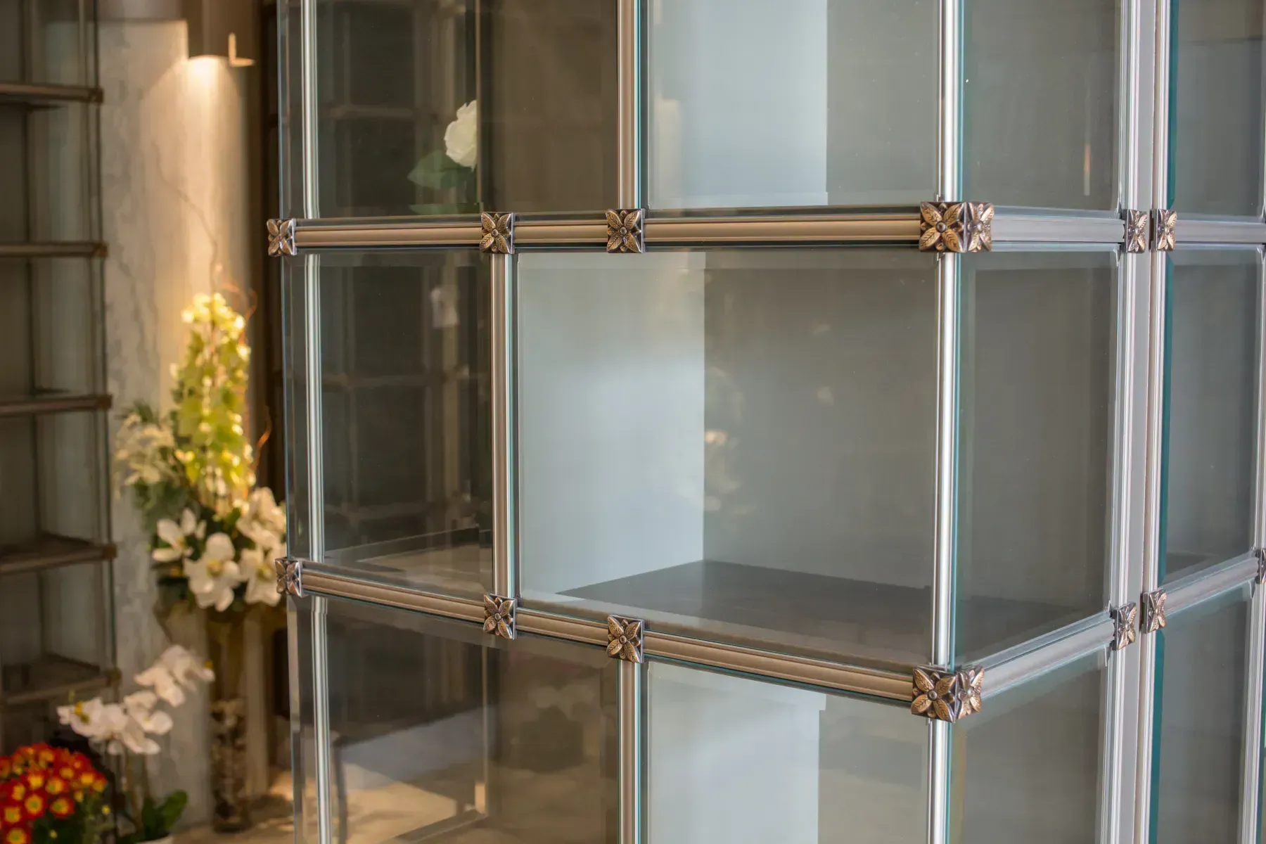 Glass shelving unit with metal frame beside a floral arrangement indoors