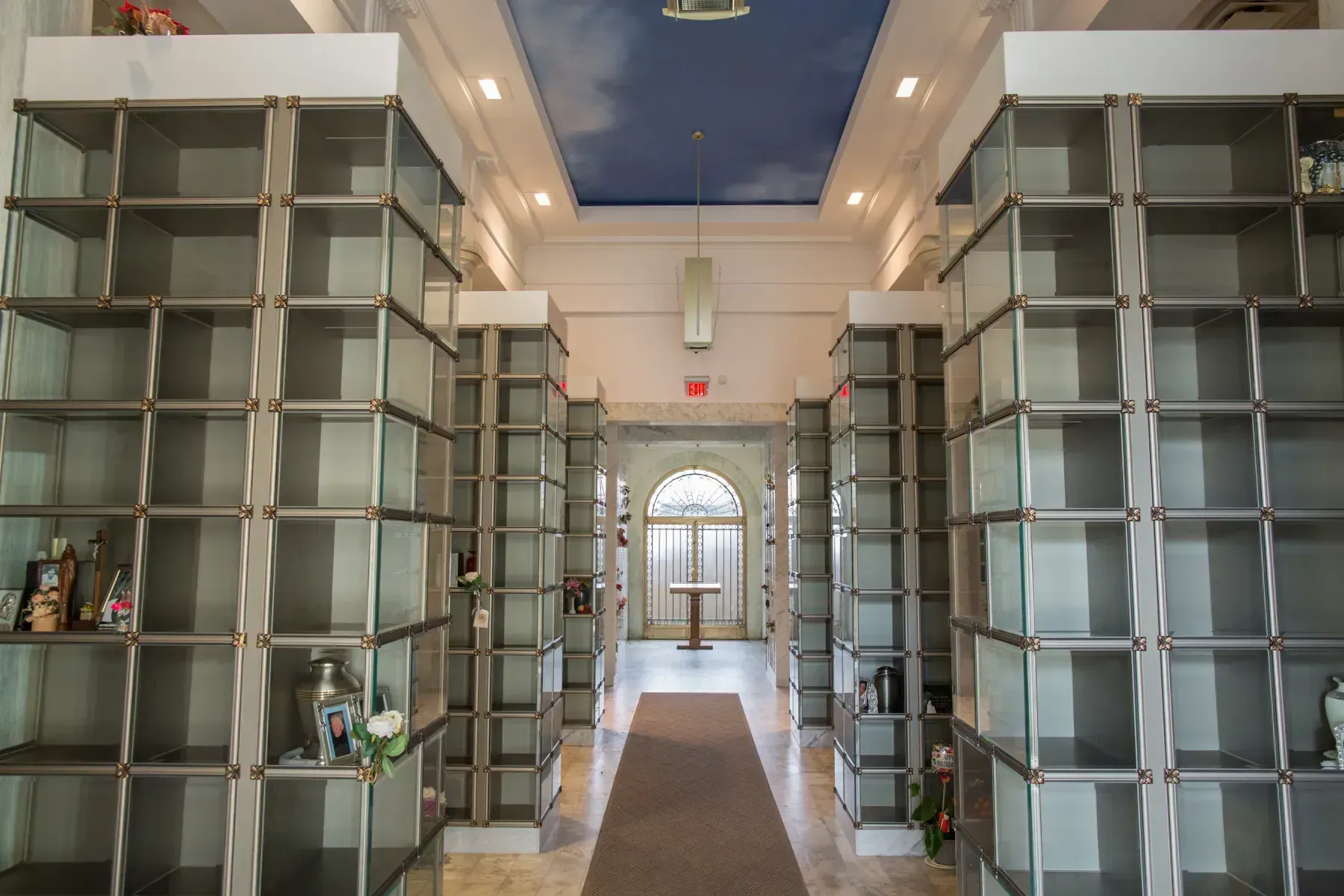 A bright hallway with tall glass shelving units lining both sides and an arched doorway at the far end.