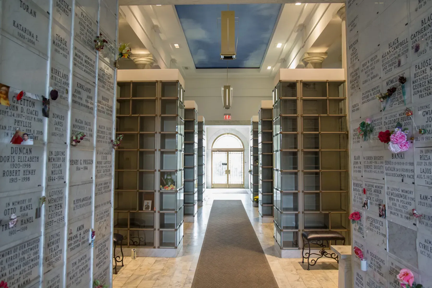 Long hallway with tall shelves and walls covered in notes, leading to a bright arched doorway.