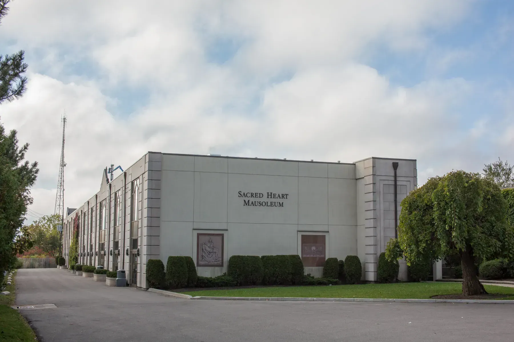 Exterior of a white church building with a parking lot and trees under a cloudy sky