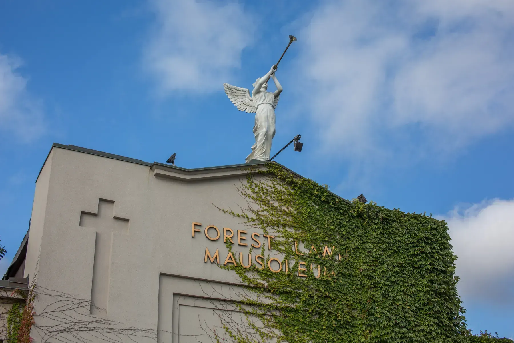 Building facade with ivy, crowned by a statue holding a trumpet against a blue sky
