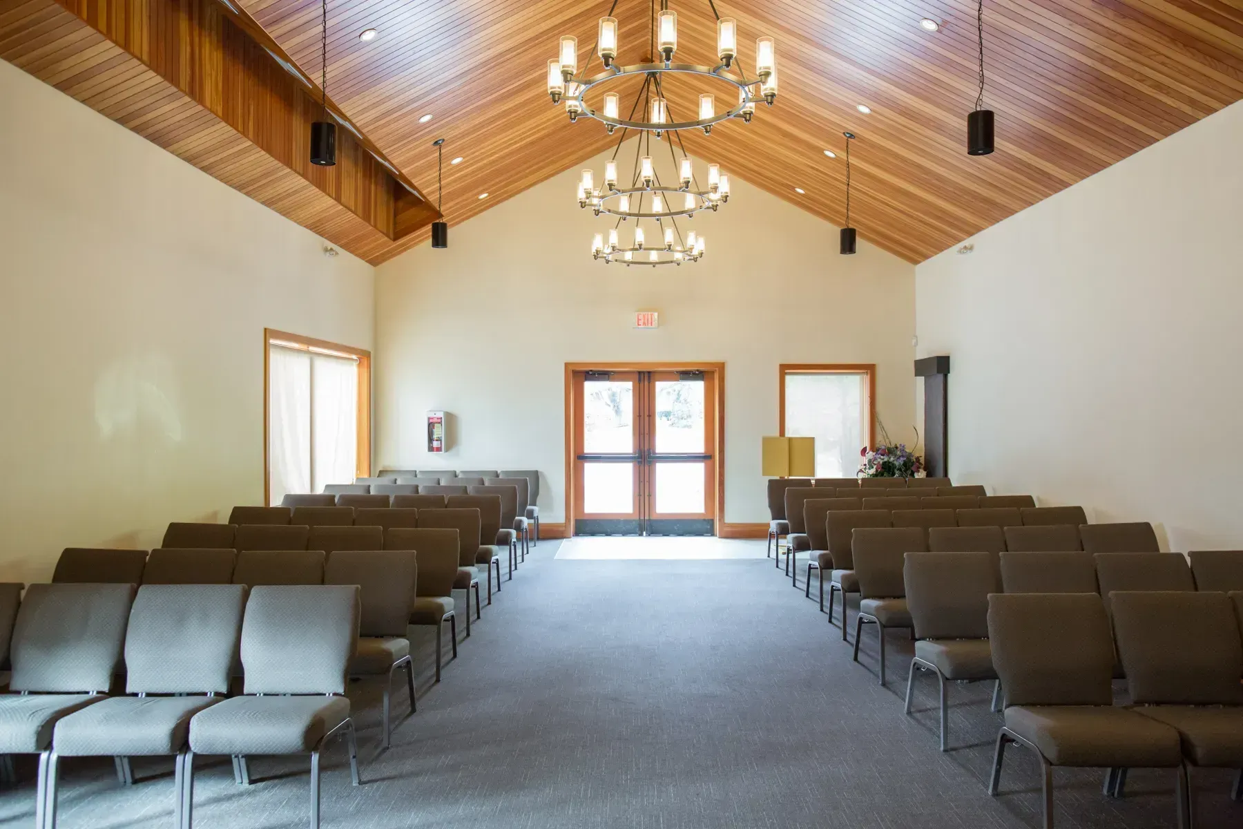 Empty church sanctuary with rows of brown chairs, chandeliers, and wooden vaulted ceiling.