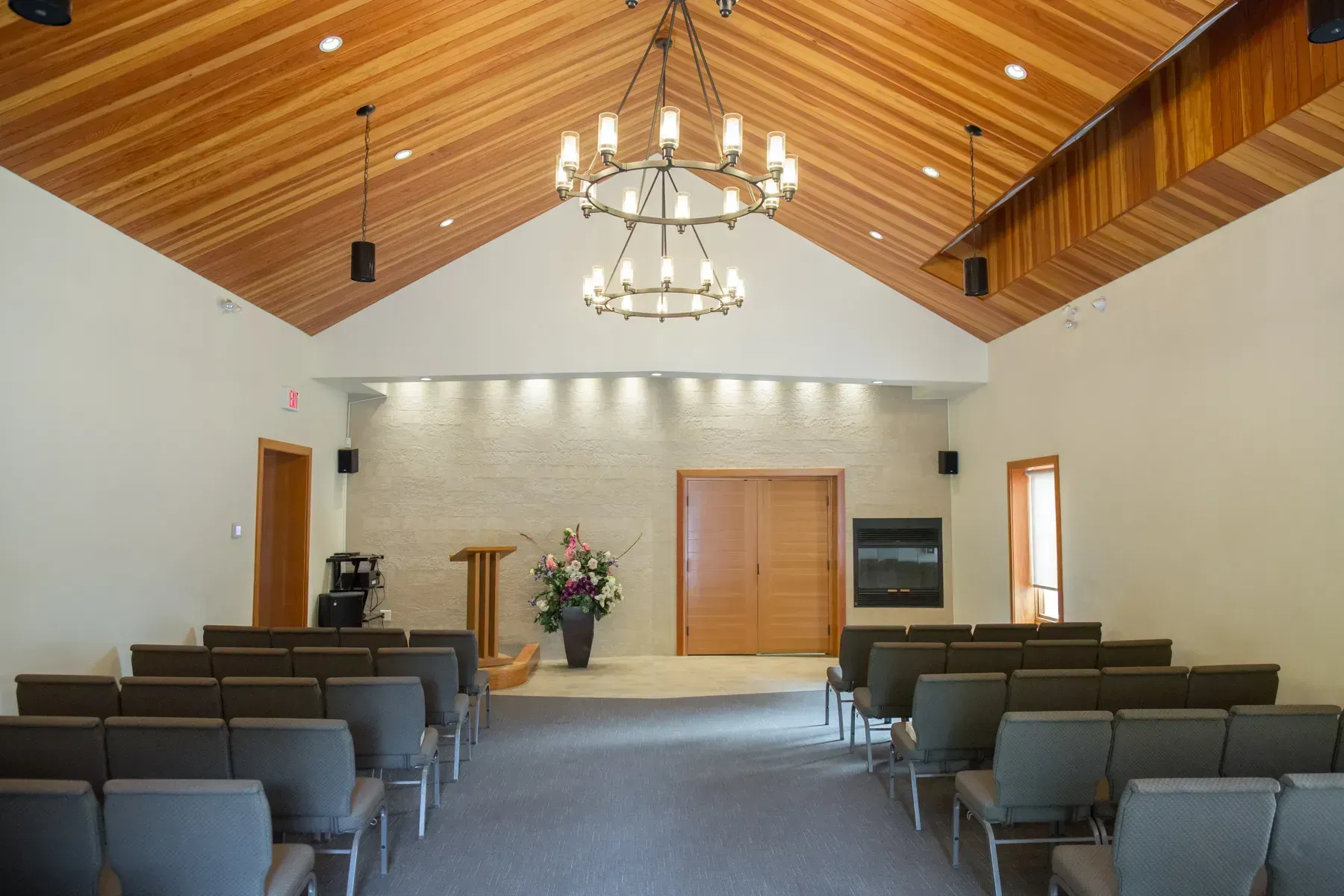Empty church sanctuary with rows of chairs, wooden vaulted ceiling, and a chandelier over the aisle