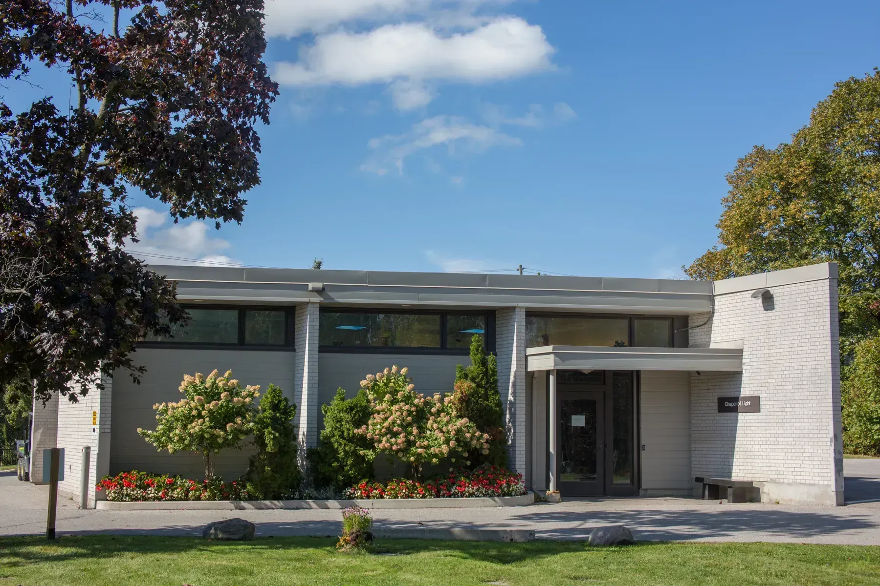 Modern single-story building with large windows, white columns, and landscaped front lawn under a blue sky