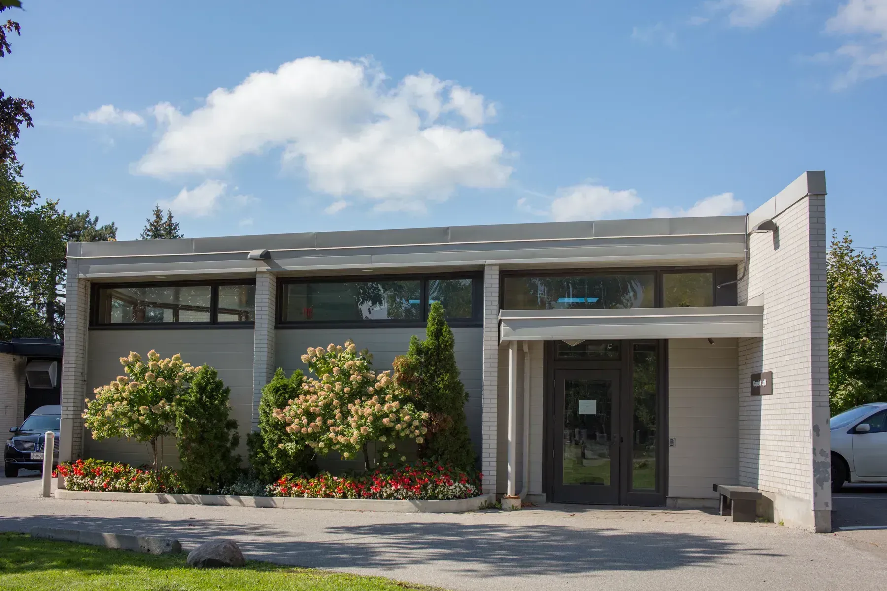 Modern one-story office building with glass entrance, gray facade, and landscaped shrubs under a blue sky