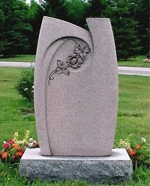 Modern abstract stone monument with floral carving on a gray base in a grassy outdoor setting