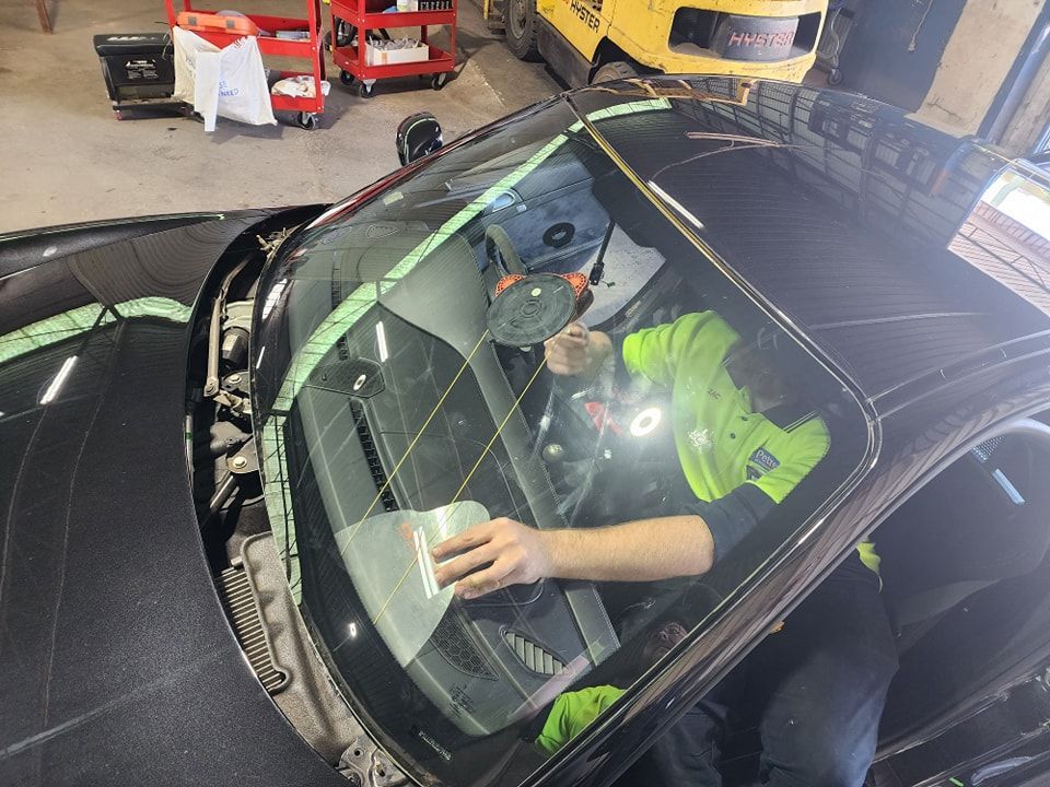 A Man Is Cleaning The Windshield Of A Car In A Garage — Petrena Windscreens In Leyburn, QLD