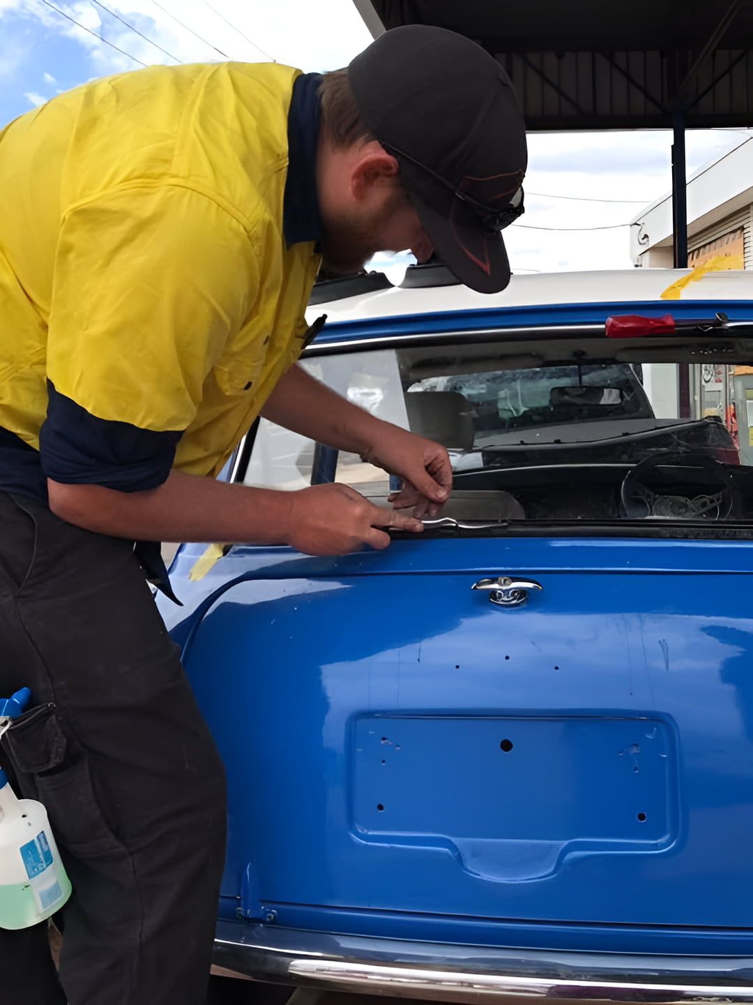 A Man In A Yellow Shirt Is Working On A Blue Car — Petrena Windscreens In Toowoomba City, QLD