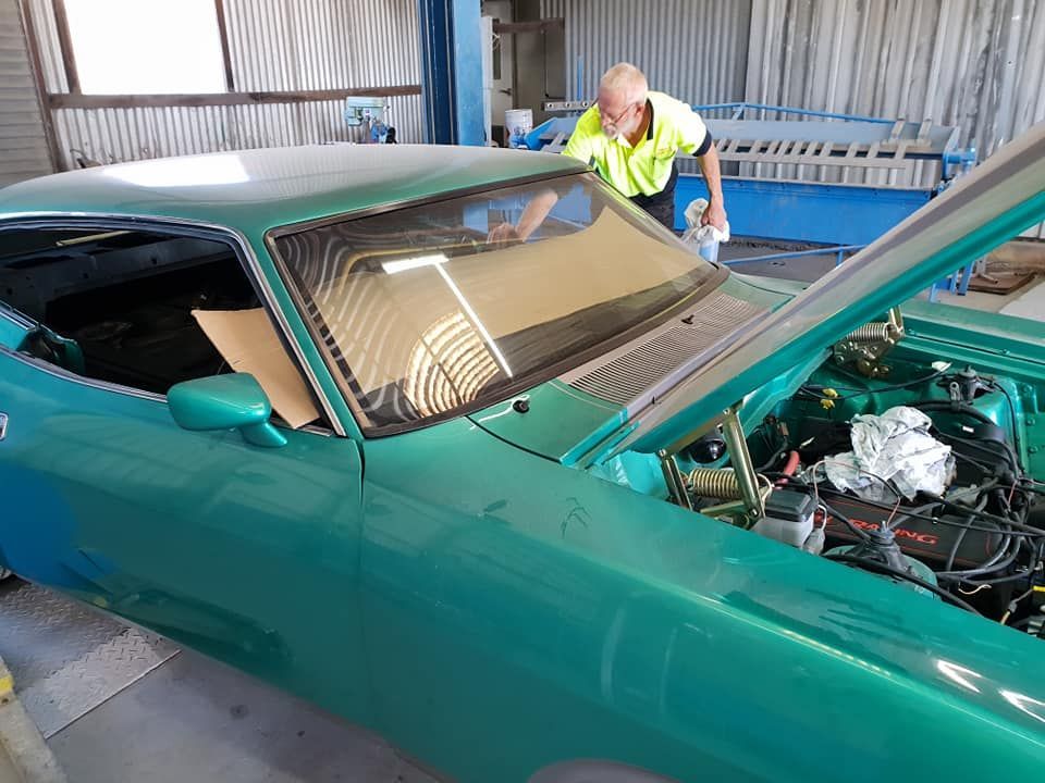 A Man Is Working On A Green Car In A Garage — Petrena Windscreens In Cambooya, QLD