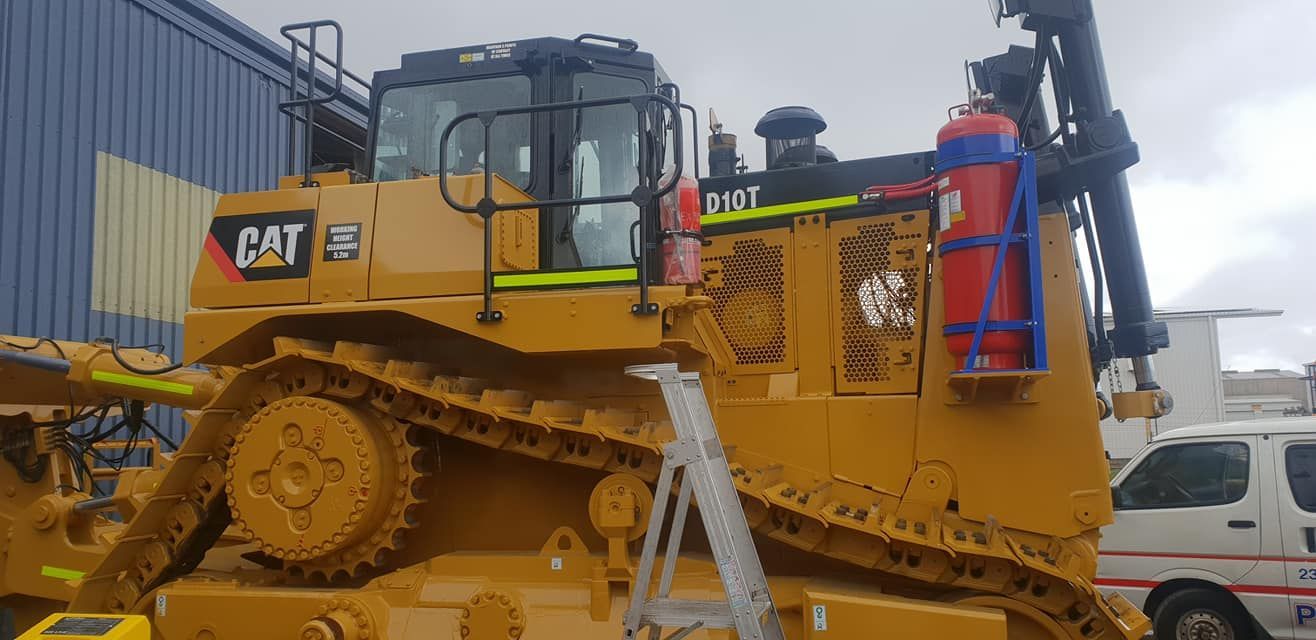 A Large Yellow Bulldozer Is Parked In Front Of A Building — Petrena Windscreens In Allora, QLD